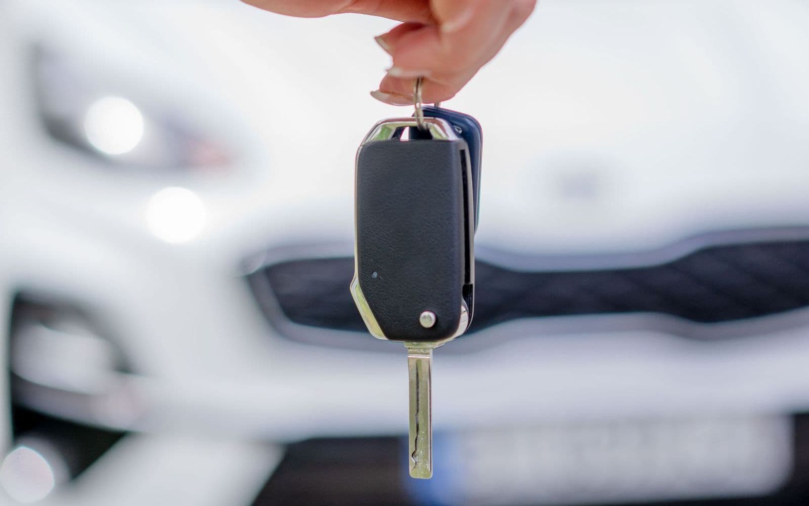 A hand holding a car key with the rental vehicle waiting in the background